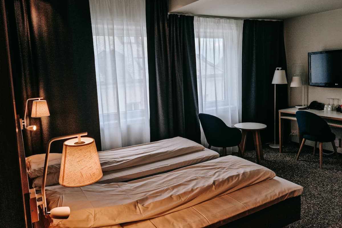 A hotel room with a bed, a desk, two chairs, a TV, and a lamp.