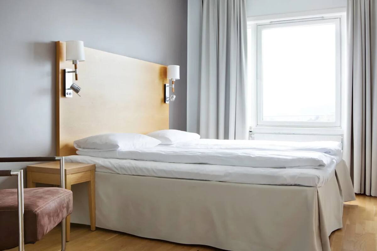 A hotel room with a bed, bedside tables, a lamp, and a window with curtains.