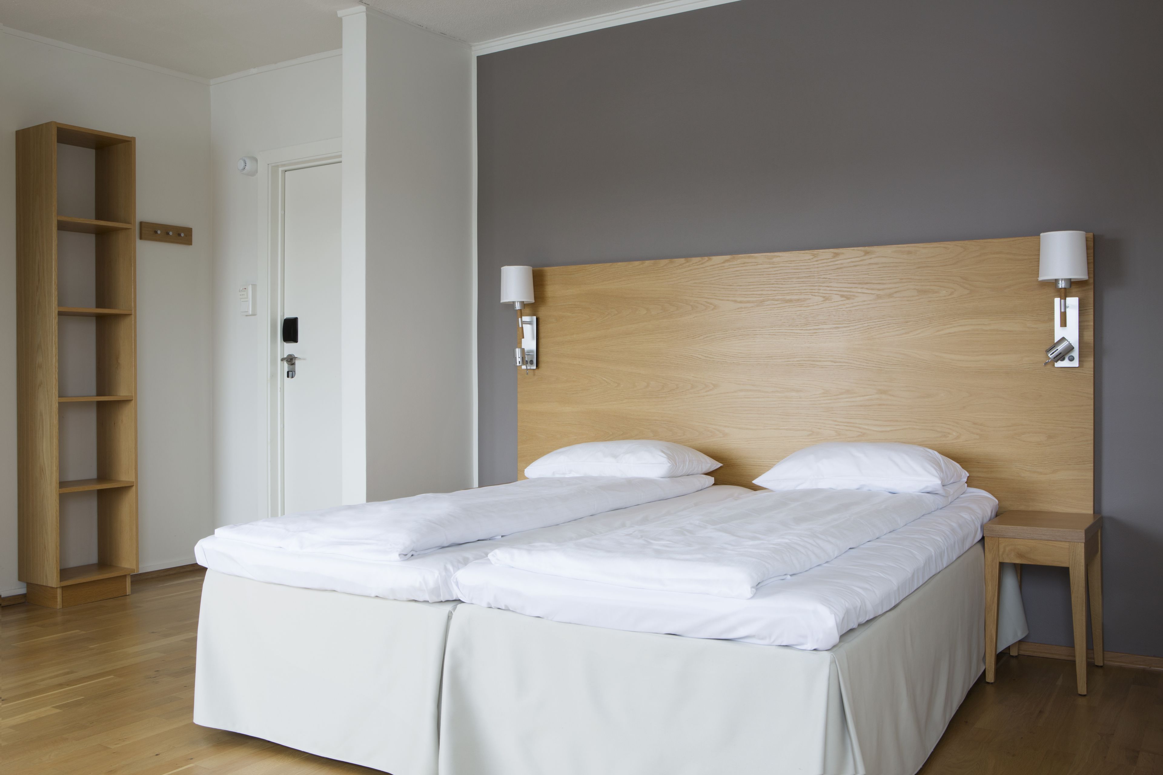 A neatly made double bed with white linens, a wooden headboard, two bedside lamps, and a wooden nightstand.
