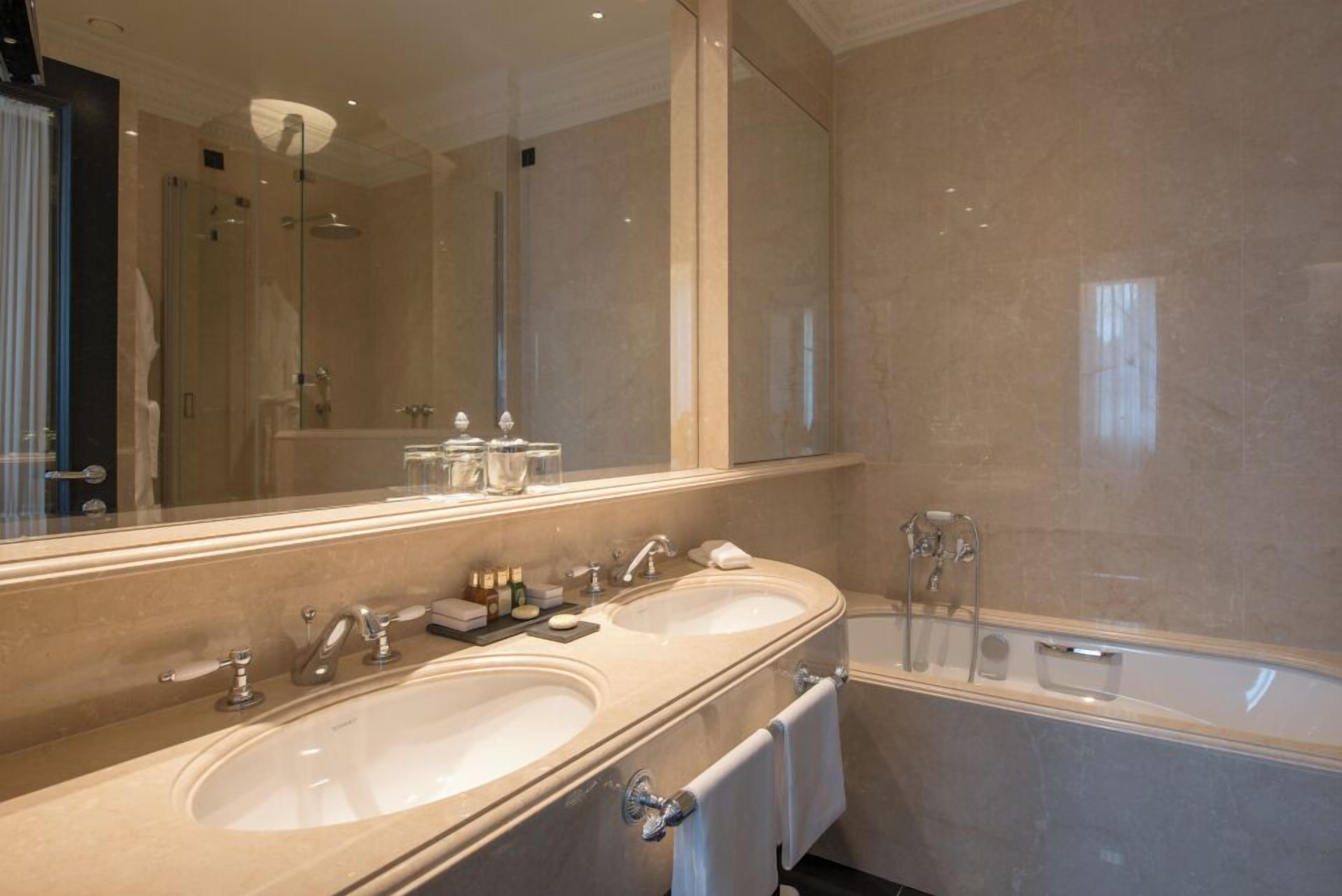 A modern bathroom with two sinks, a large mirror, and a bathtub.