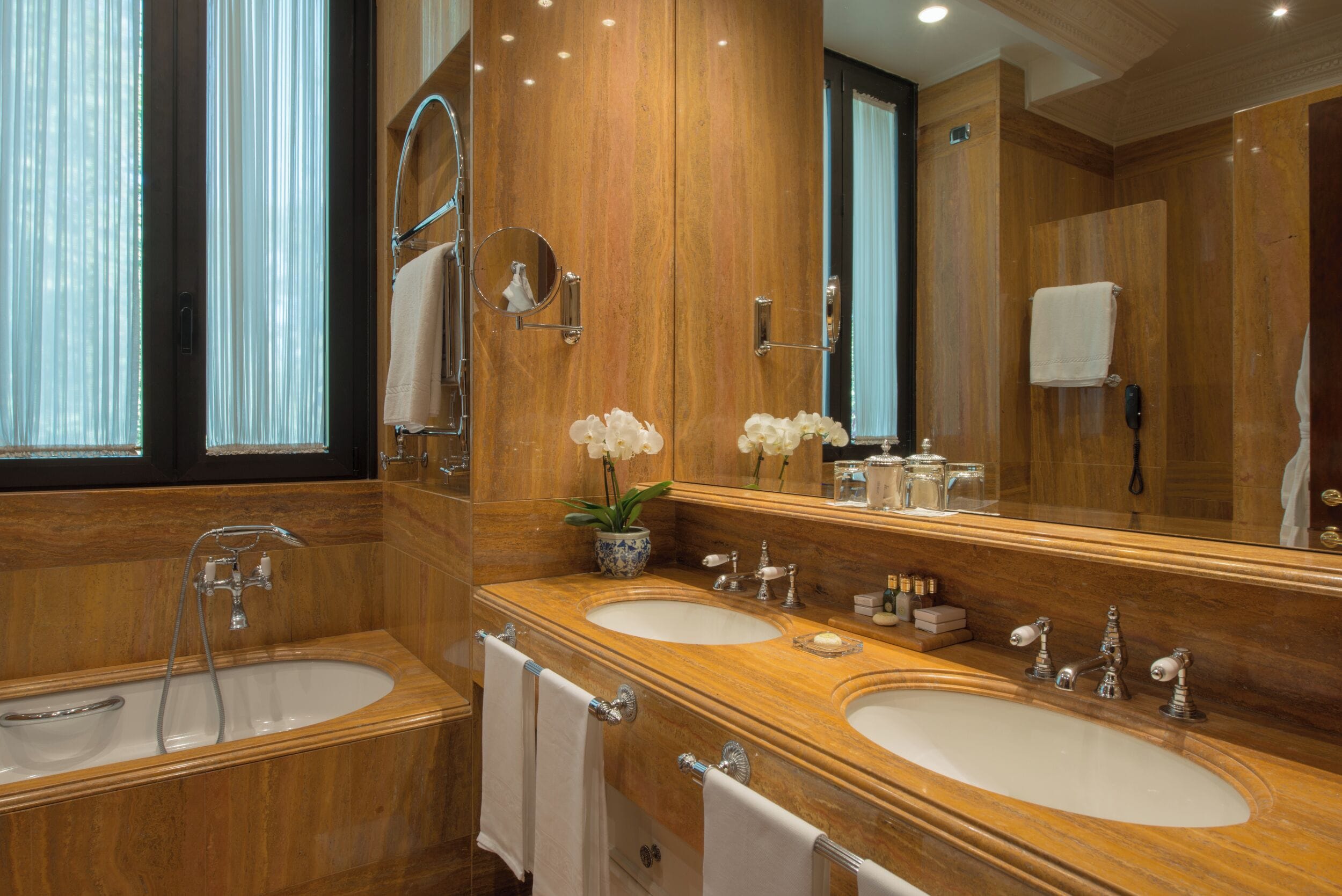 A luxurious bathroom with two sinks, a large mirror, and a potted plant.