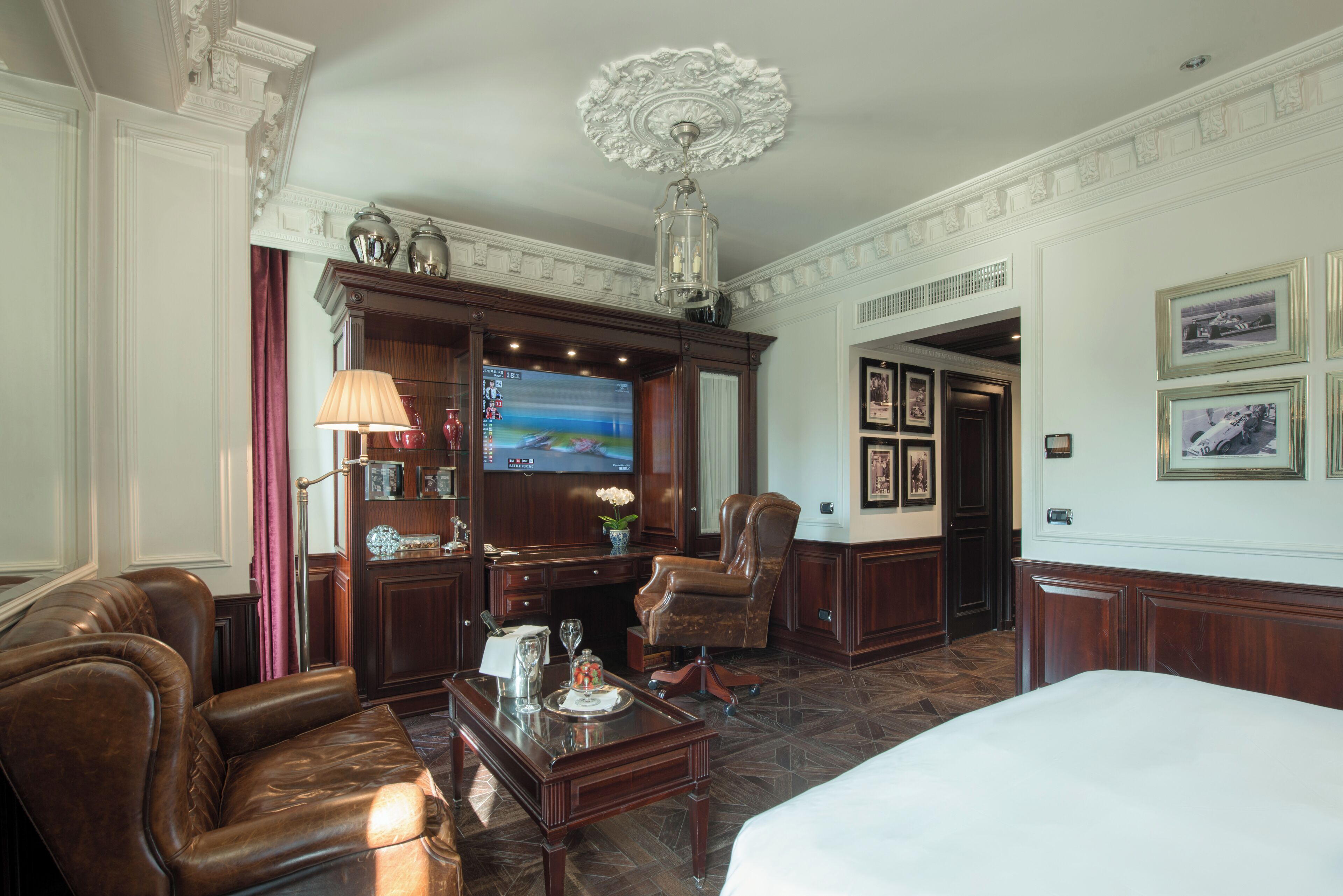 A hotel room with a large bed, leather armchairs, a wooden desk, a television, and framed pictures on the wall.