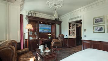 Une chambre d’hôtel avec un grand lit, des fauteuils en cuir, un bureau en bois, une télévision et des tableaux encadrés au mur.