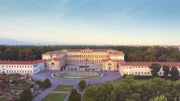 A large, symmetrical building with a central courtyard, surrounded by manicured gardens and trees.