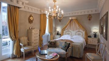 Um quarto luxuoso com uma cama de dossel, uma poltrona, um laptop sobre uma mesinha e uma mesa de cabeceira com abajur.