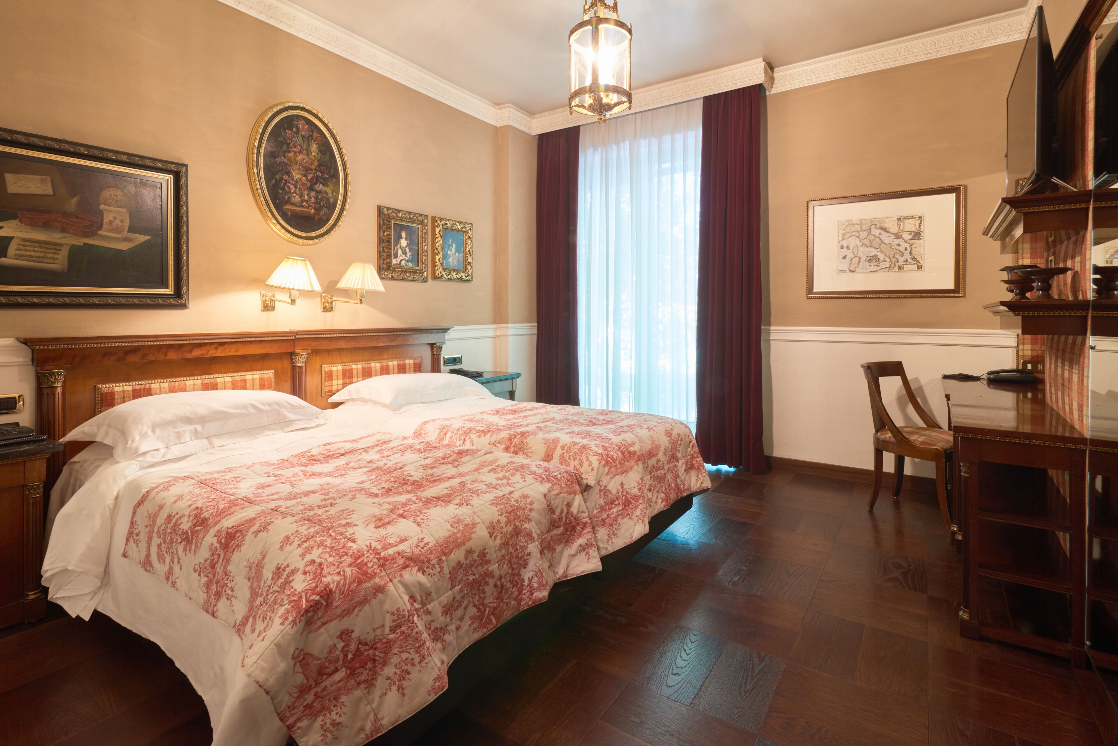 Ein Hotelzimmer mit einem großen Bett, zwei Nachttischlampen, einem Holfnachtkästchen, einem Sessel, einem Schreibtisch und einem großen Fenster mit Vorhängen.