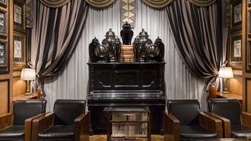 A room with a piano, leather chairs, a glass coffee table, and a bookshelf.