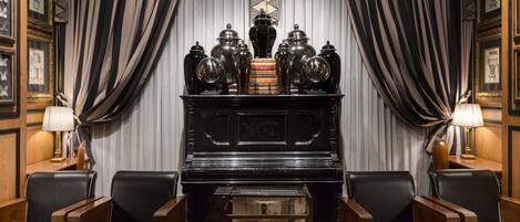 Una habitación con un piano, sillones de cuero, una mesa de centro de vidrio y una estantería.