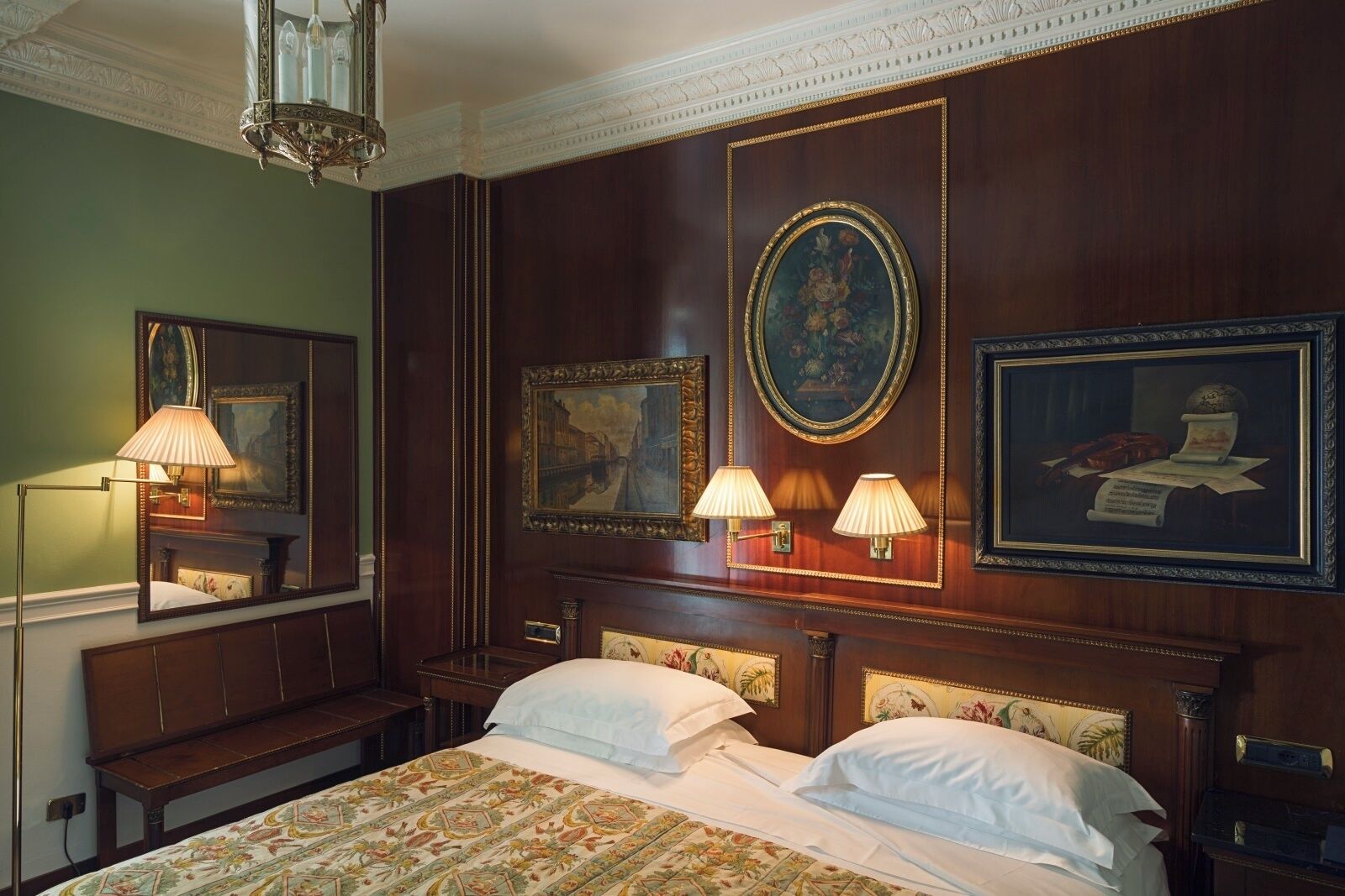 Ein Hotelzimmer mit einem großen Bett, zwei Nachttischlampen, einem Spiegel und gerahmten Kunstwerken an den Wänden.