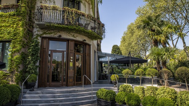 A building with a curved entrance, steps leading up to it, and a balcony with plants.