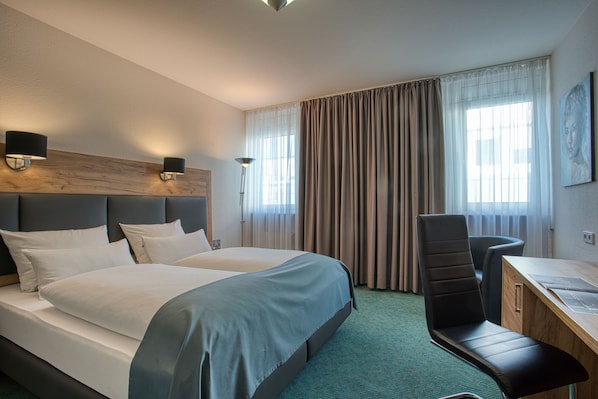 Habitación de hotel con una cama grande, dos mesitas de noche con lámparas, un escritorio con silla y vistas al exterior por la ventana.