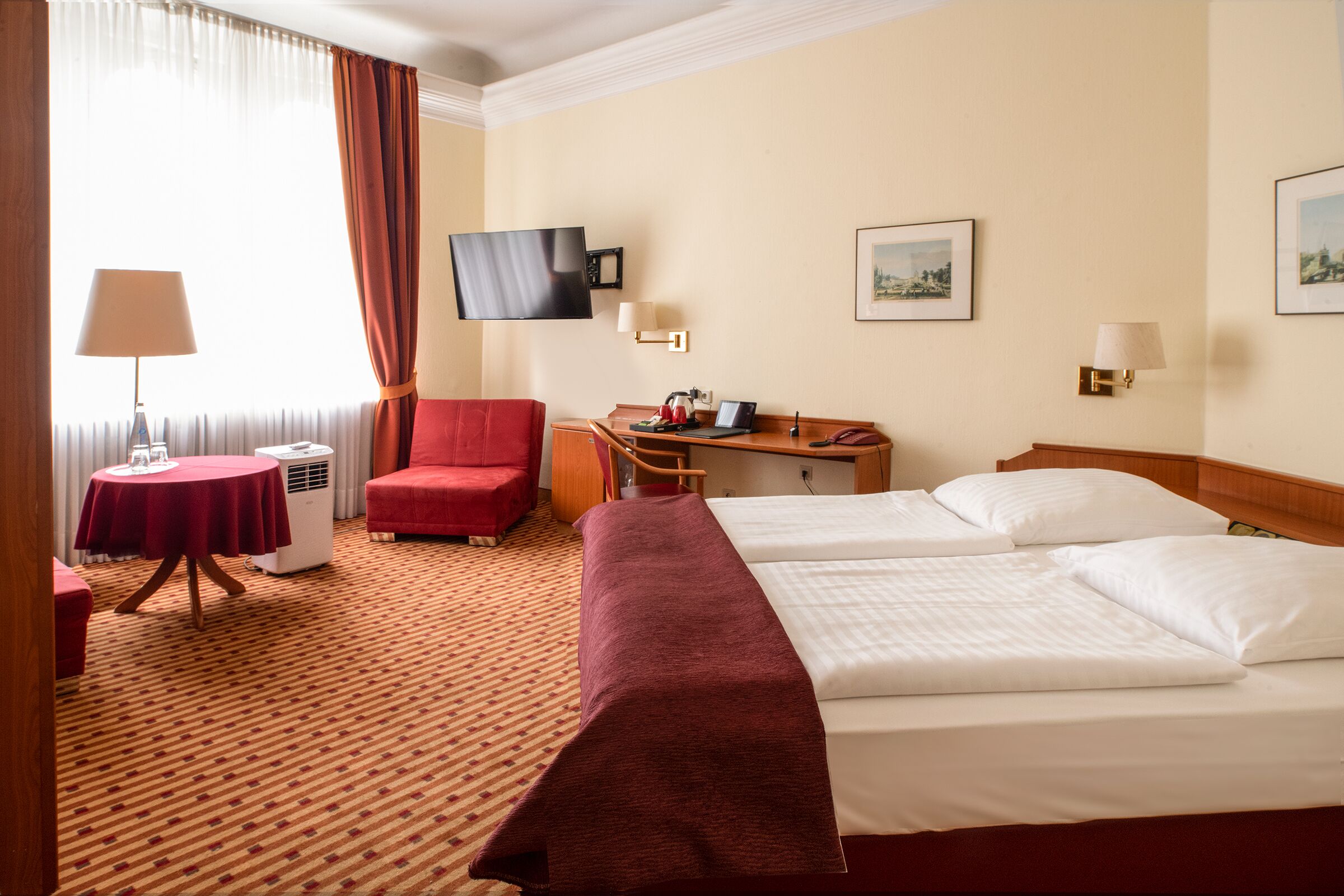 Ein Hotelzimmer mit Bett, Schreibtisch, Stuhl, Fernseher und einem Fenster mit Vorhängen.