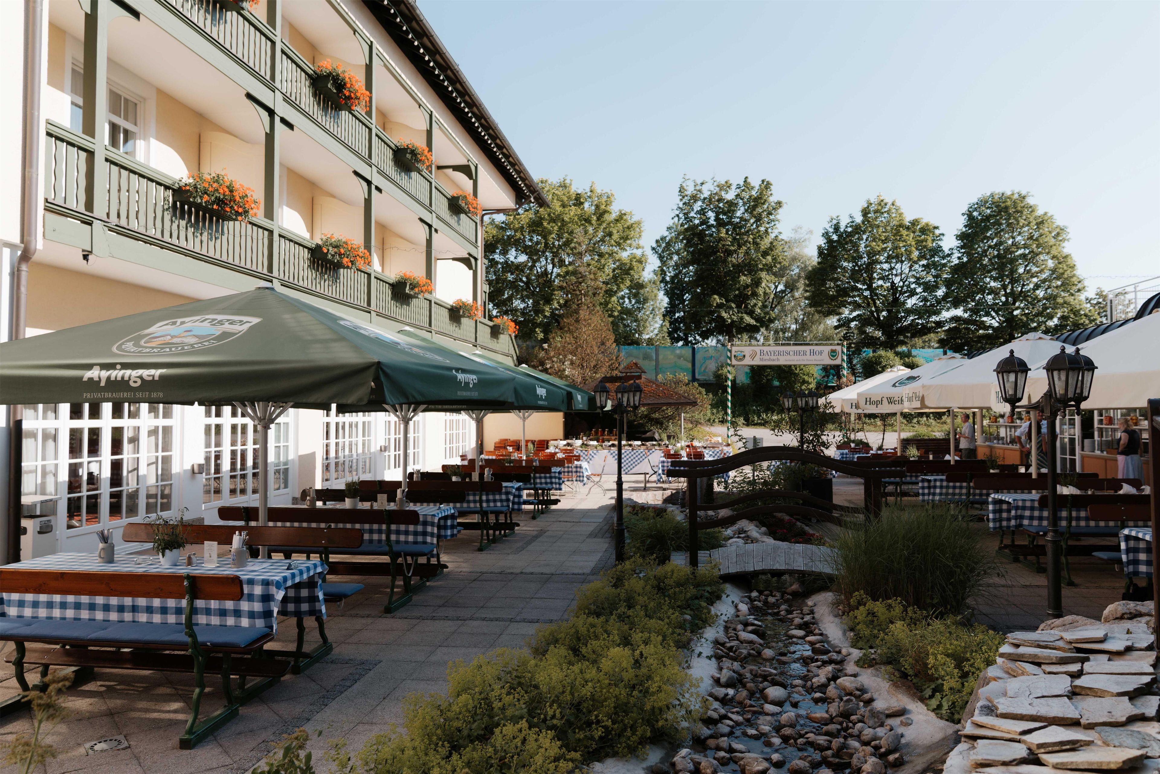 An outdoor seating area with tables and benches, a stone pathway, and a building with balconies.
