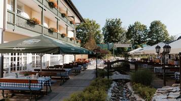 An outdoor seating area with tables and benches, a stone pathway, and a building with balconies.