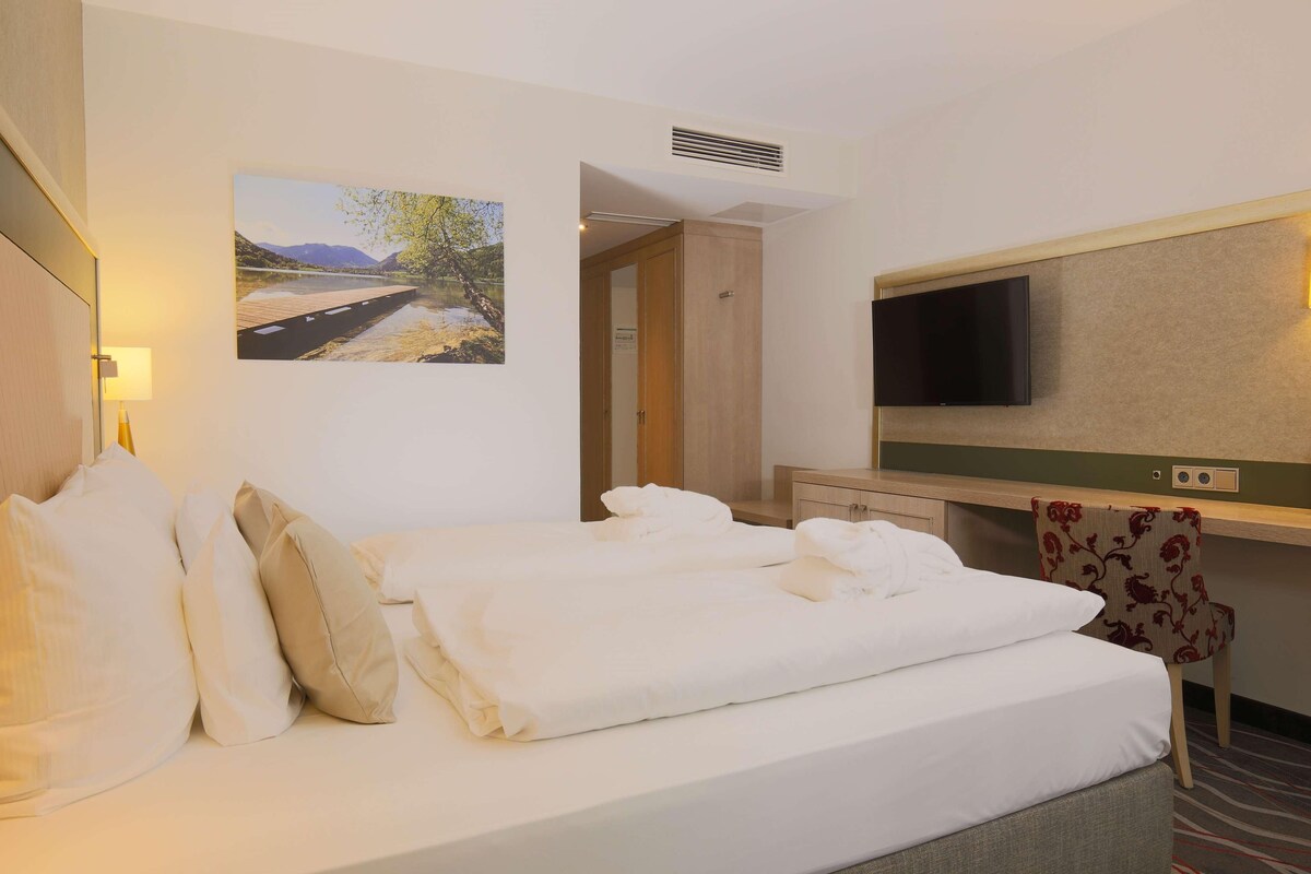 Ein Hotelzimmer mit Bett, Flachbildfernseher, Wandgemälde und einer Tür zu einem weiteren Raum.