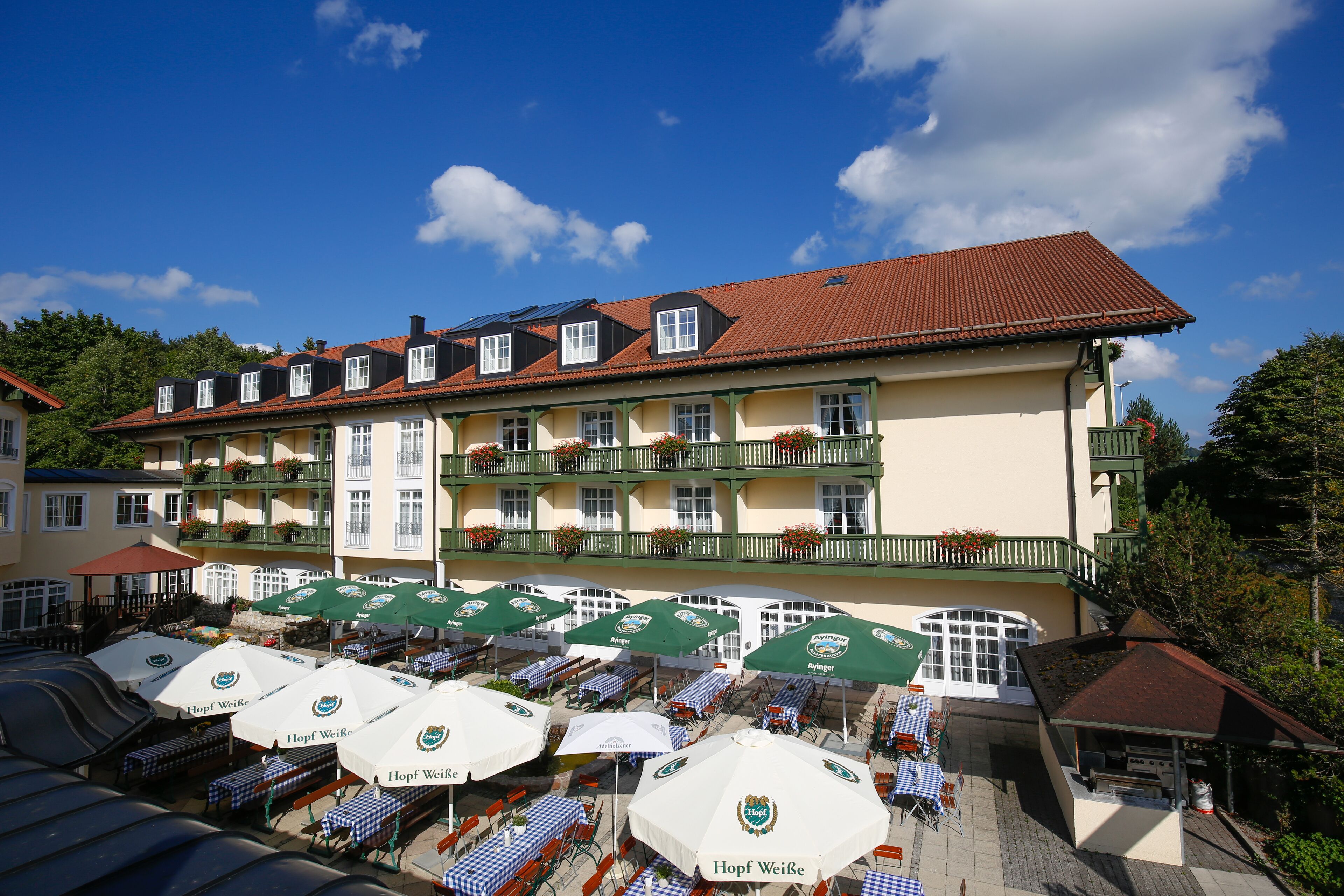 A hotel with outdoor seating and multiple umbrellas, featuring a traditional European architectural style.