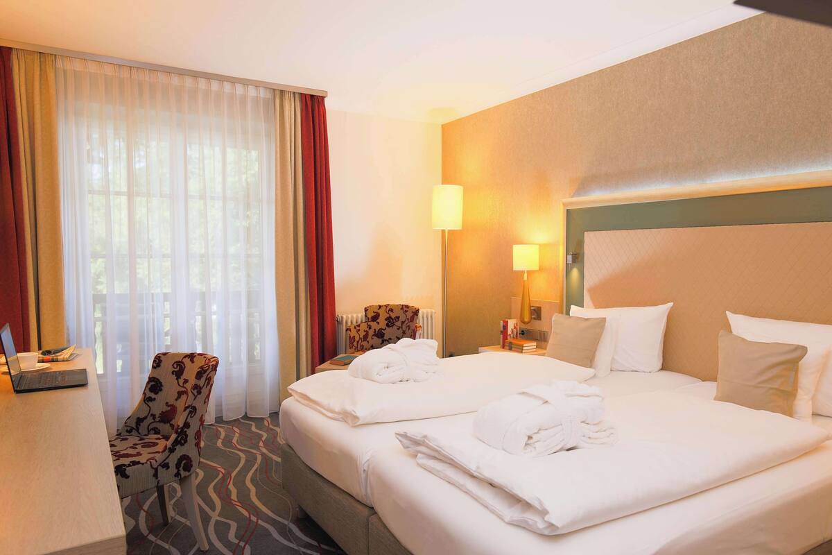 A hotel room with a bed, a desk, a chair, and a window with curtains.