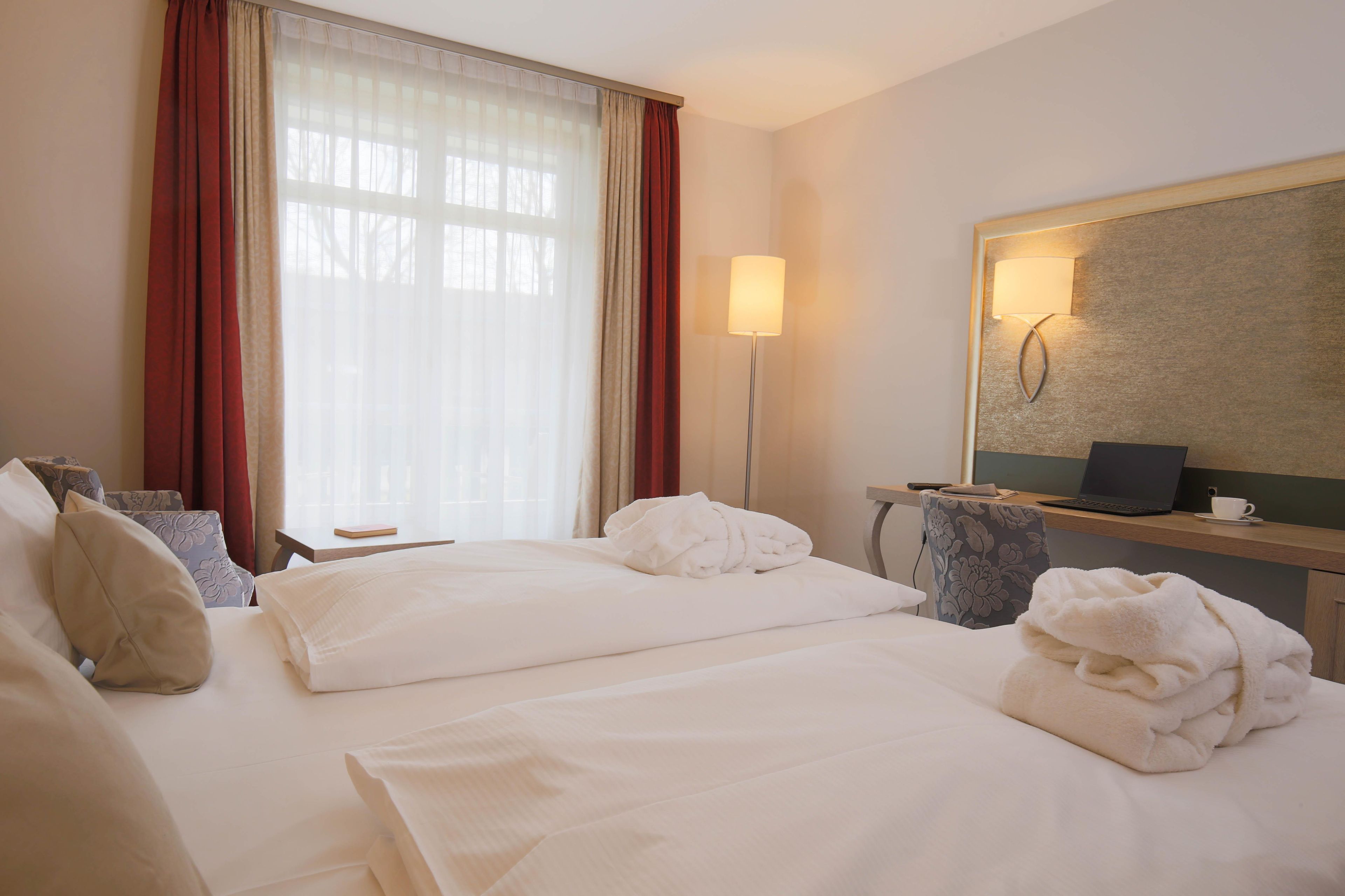 Une chambre d’hôtel avec deux lits, un bureau, une chaise, une lampe et un grand miroir.