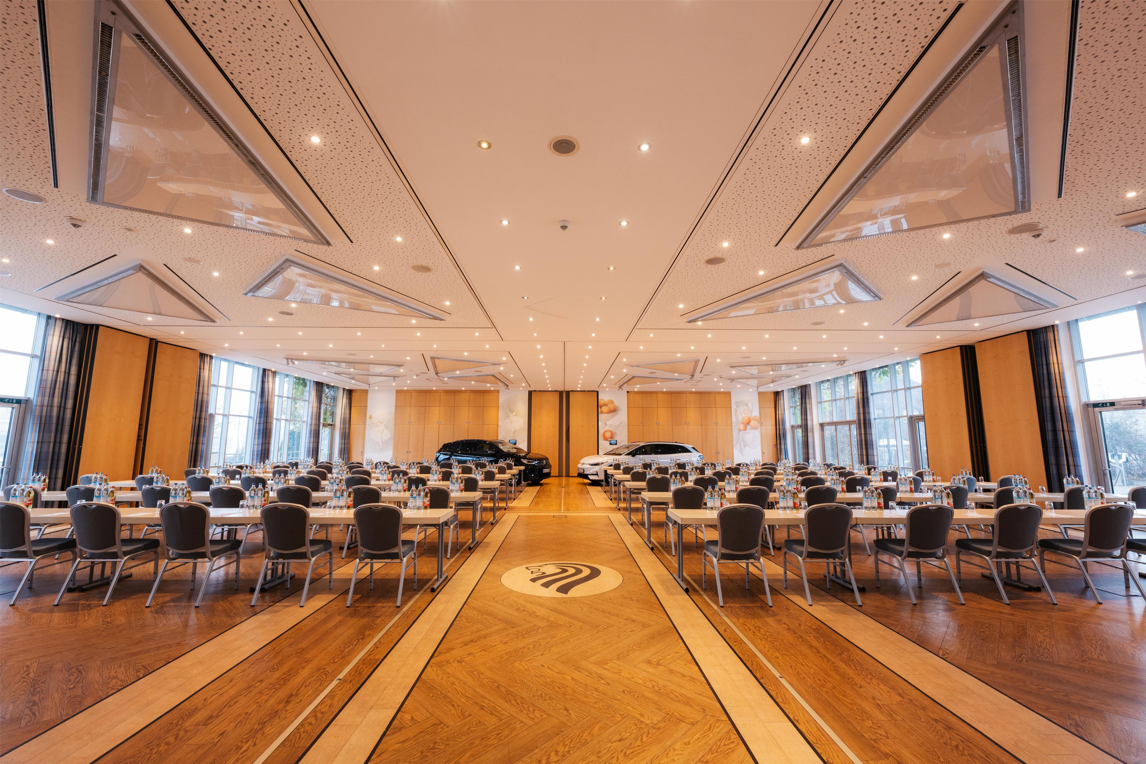 A spacious conference room with multiple tables and chairs, large windows, and a central logo on the floor.
