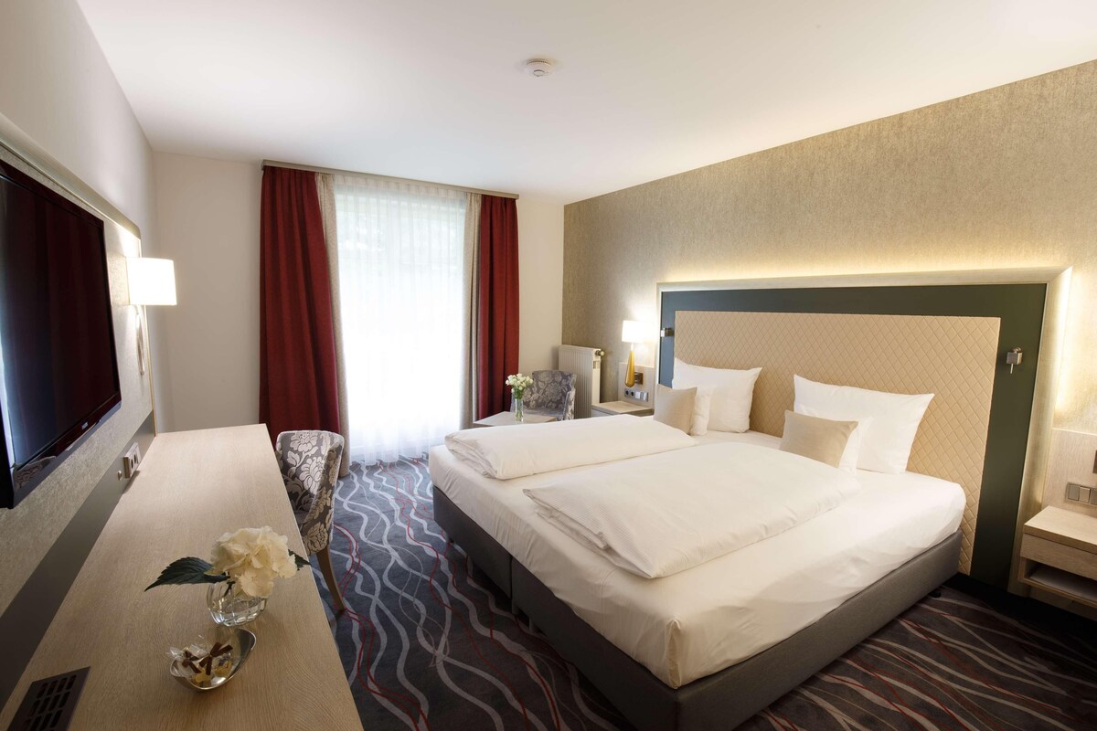 Ein Hotelzimmer mit Bett, Nachttischen, Schreibtisch und Stuhl.