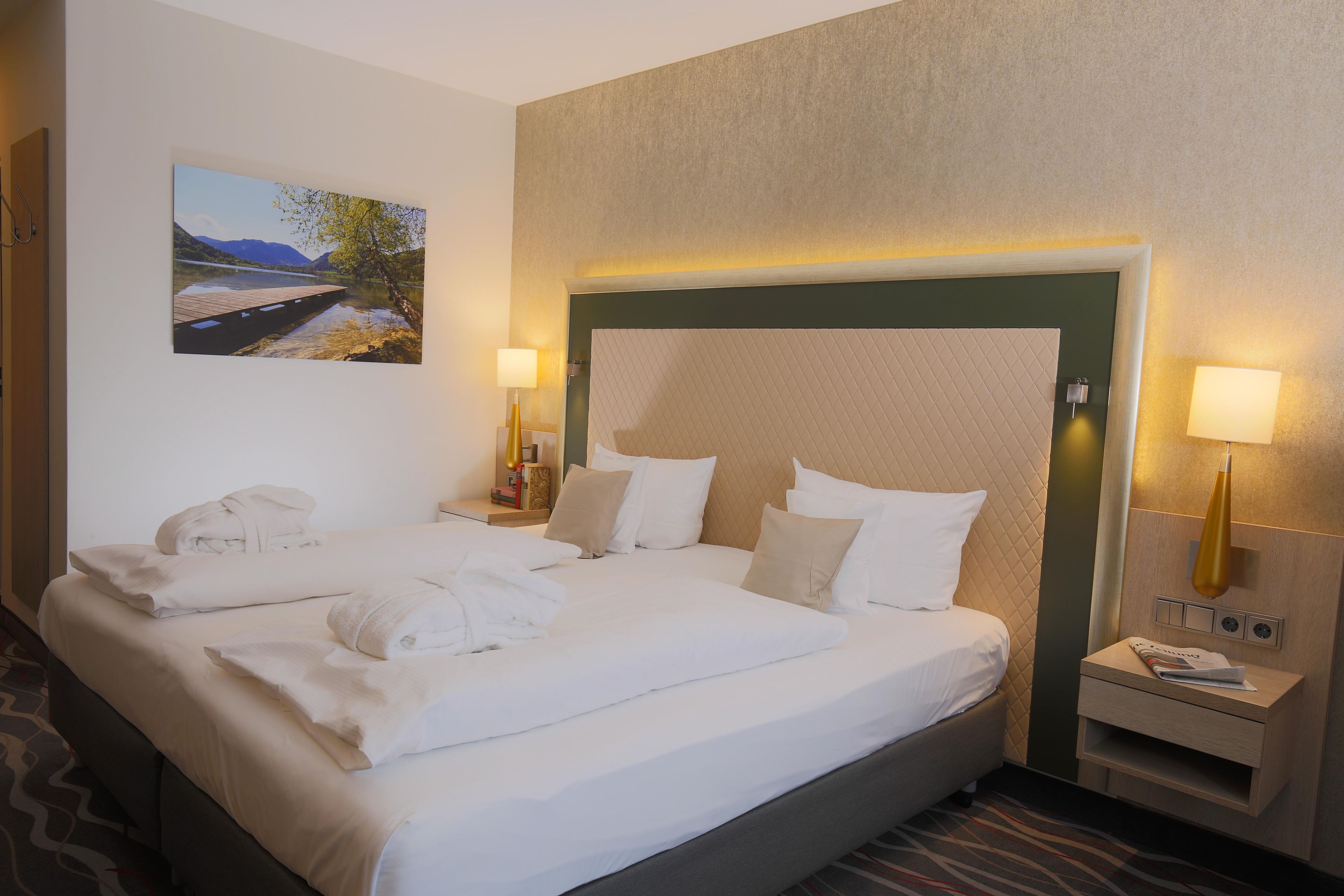 Ein Hotelzimmer mit zwei Betten, einem Landschaftsbild und einem Nachttisch mit einer Lampe.