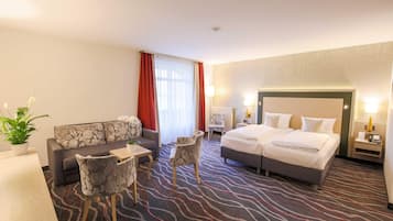 Ein Hotelzimmer mit einer Couch, zwei Sessel, einem kleinen Tisch, einem Bett und einem Nachttisch mit Lampe.