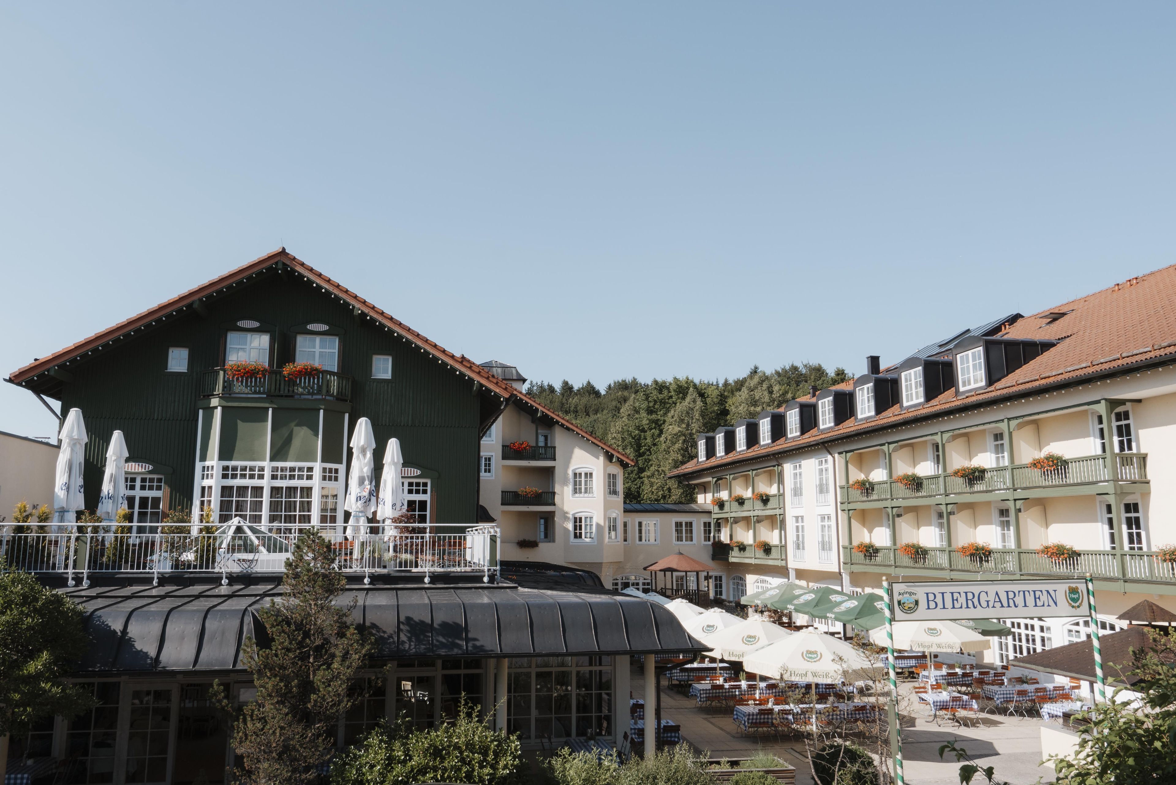 A traditional European building with a green facade, multiple balconies with flower boxes, and outdoor seating areas with umbrellas.