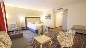 A hotel room with a bed, a sofa, a chair, a small table with a plant, and a bench. - Hotel Bayerischer Hof Miesbach, BW Premier Collection (Miesbach)
