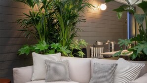En moderne stue med en sofa, mønstrede puder, et træ sofabord og store grønne planter.