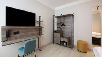 Ein modernes Schlafzimmer mit an der Wand montiertem Fernseher, einem Schreibtisch mit Stuhl, einem Kleiderschrank und einem Nachttisch.