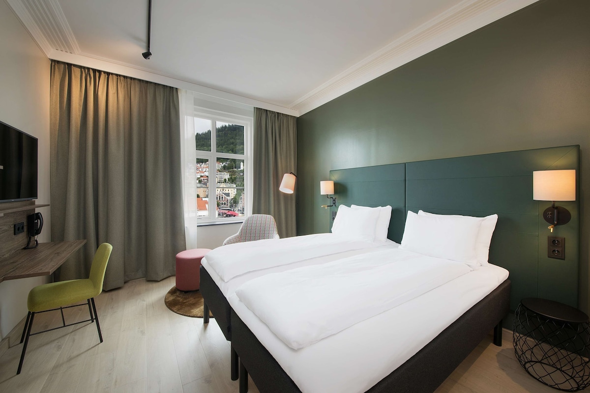 A hotel room with a bed, a desk, a chair, a round table, and a view of a cityscape.