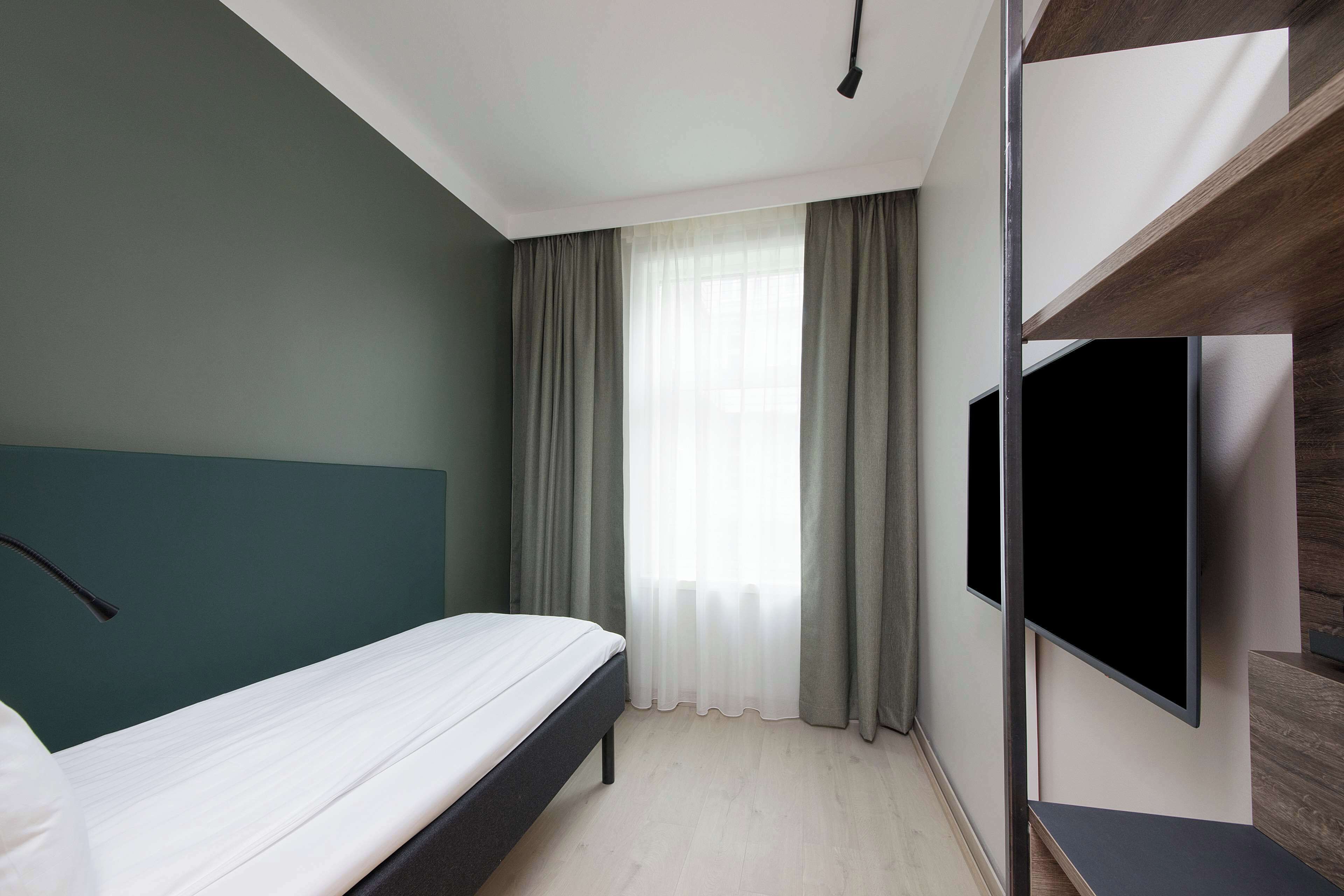 A modern hotel room with a bed, a flat-screen TV, and a large window with curtains.