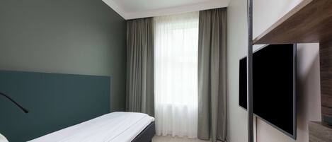 A modern hotel room with a bed, a flat-screen TV, and a large window with curtains.