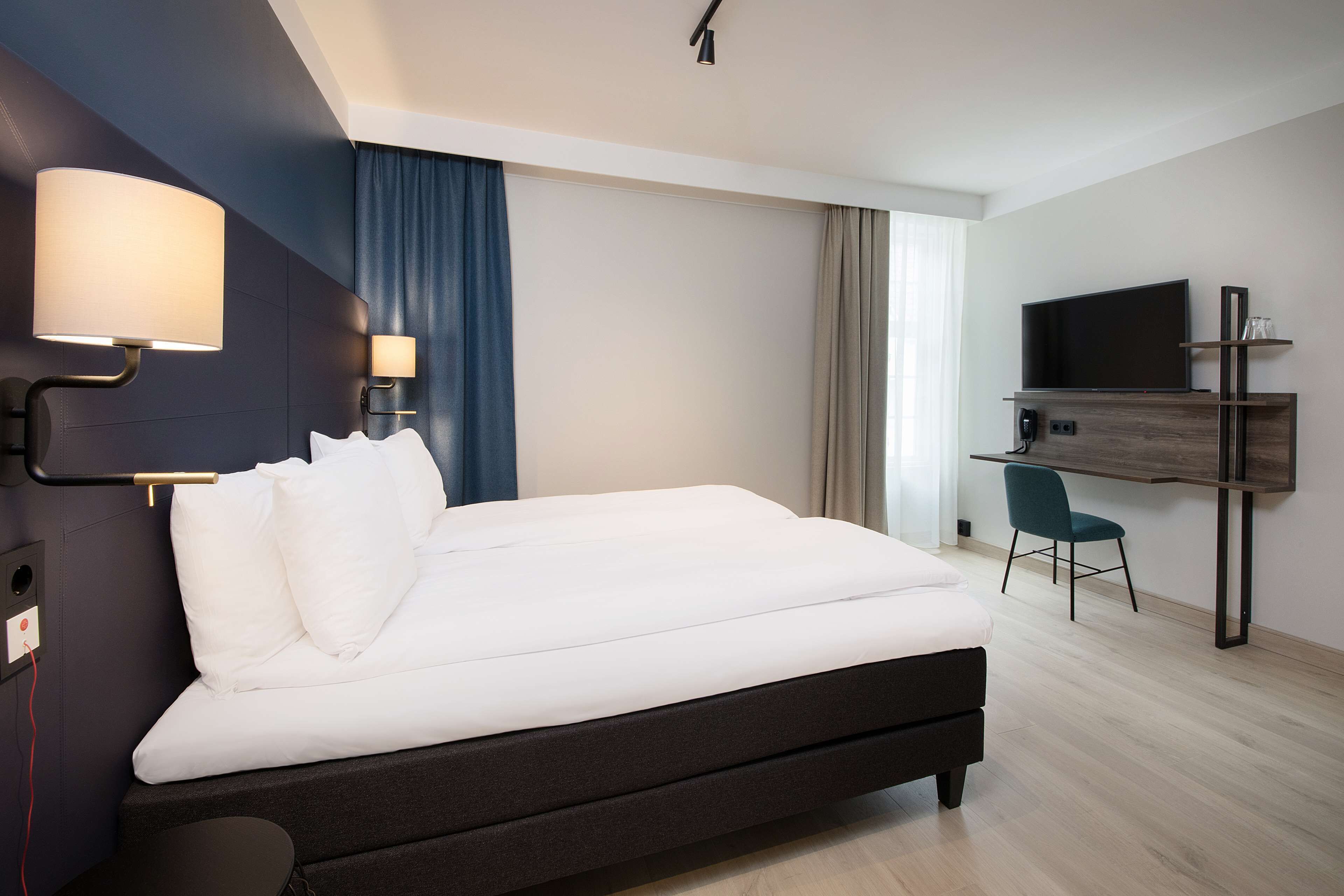 Une chambre d’hôtel moderne équipée d’un grand lit, d’un bureau, d’une chaise, d’une télévision et d’une lampe.
