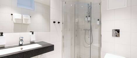 A modern bathroom with a glass-enclosed shower, a white sink with a black countertop, and a white toilet.