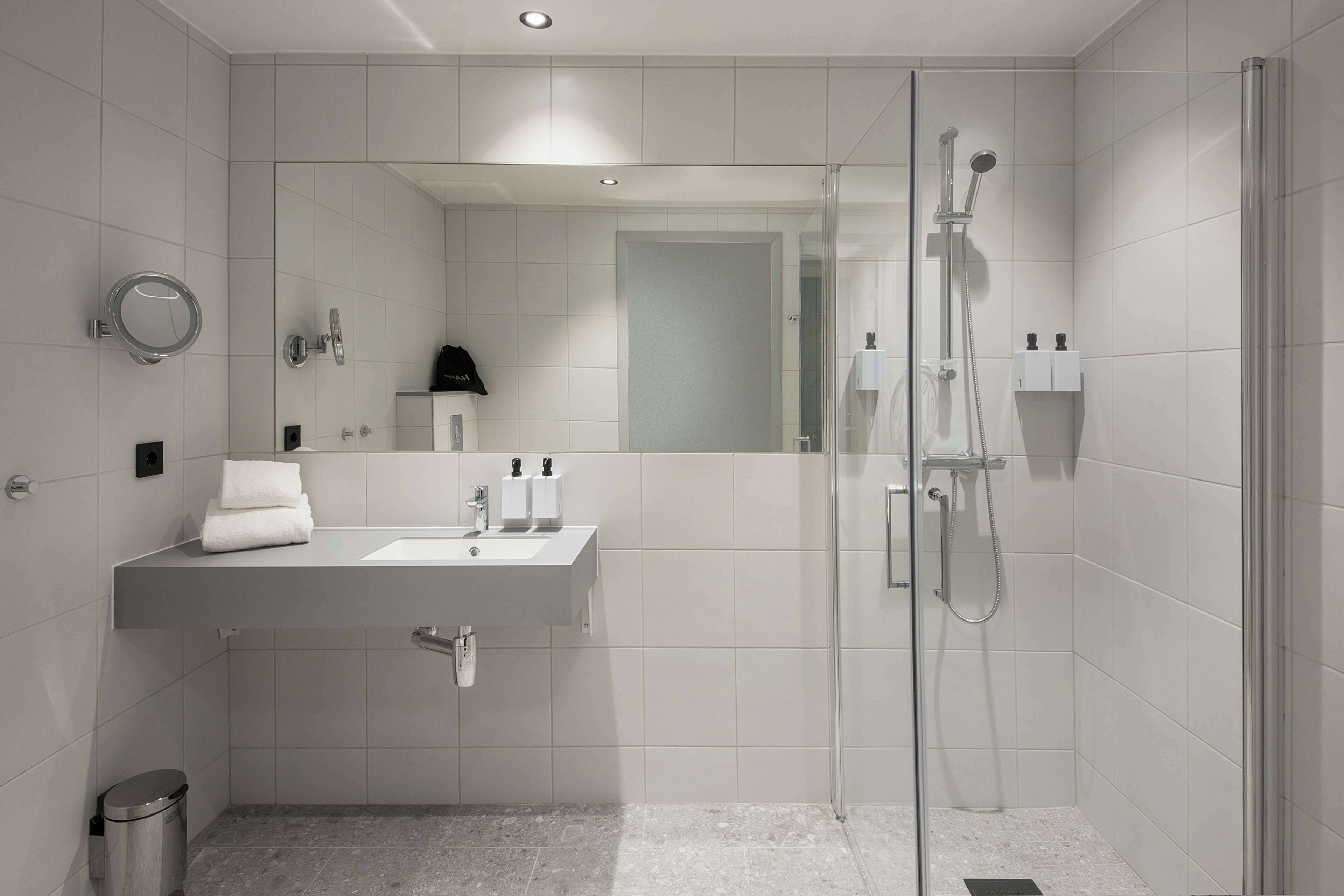 A modern bathroom with a glass-enclosed shower, a sink with a mirror, and a trash bin.