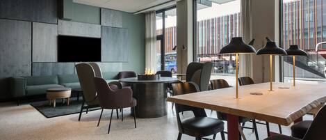 Un salón de conferencias moderno con una mesa redonda, sillas, un televisor de pantalla plana y un amplio ventanal con vistas a edificios.