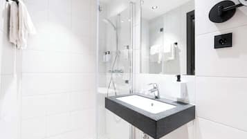 Een moderne badkamer met een douchecabine van glas, een zwart aanrechtwastafeltje en witte betegelde wanden.