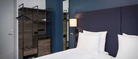 A modern hotel room with a bed, a wardrobe, and a mirror.