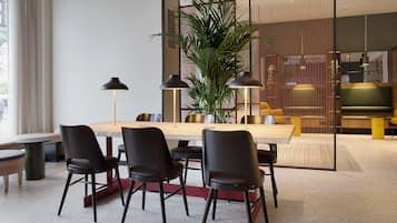 A modern dining area with a long table, black chairs, and a large potted plant.