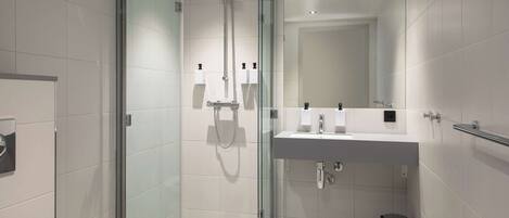 Un baño moderno con ducha de vidrio, un lavabo blanco con un espejo encima y un pequeño cubo de basura.