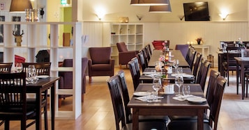 A restaurant with wooden tables and chairs, a whiteboard, and a shelf with decorative items.