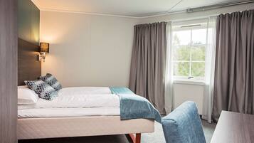A hotel room with a bed, a bedside table, a lamp, and a window with curtains.