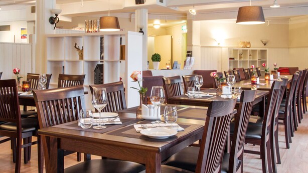 A restaurant with wooden tables and chairs, set with wine glasses and plates. - Scandic Leknes Lofoten (Vestvågøy)