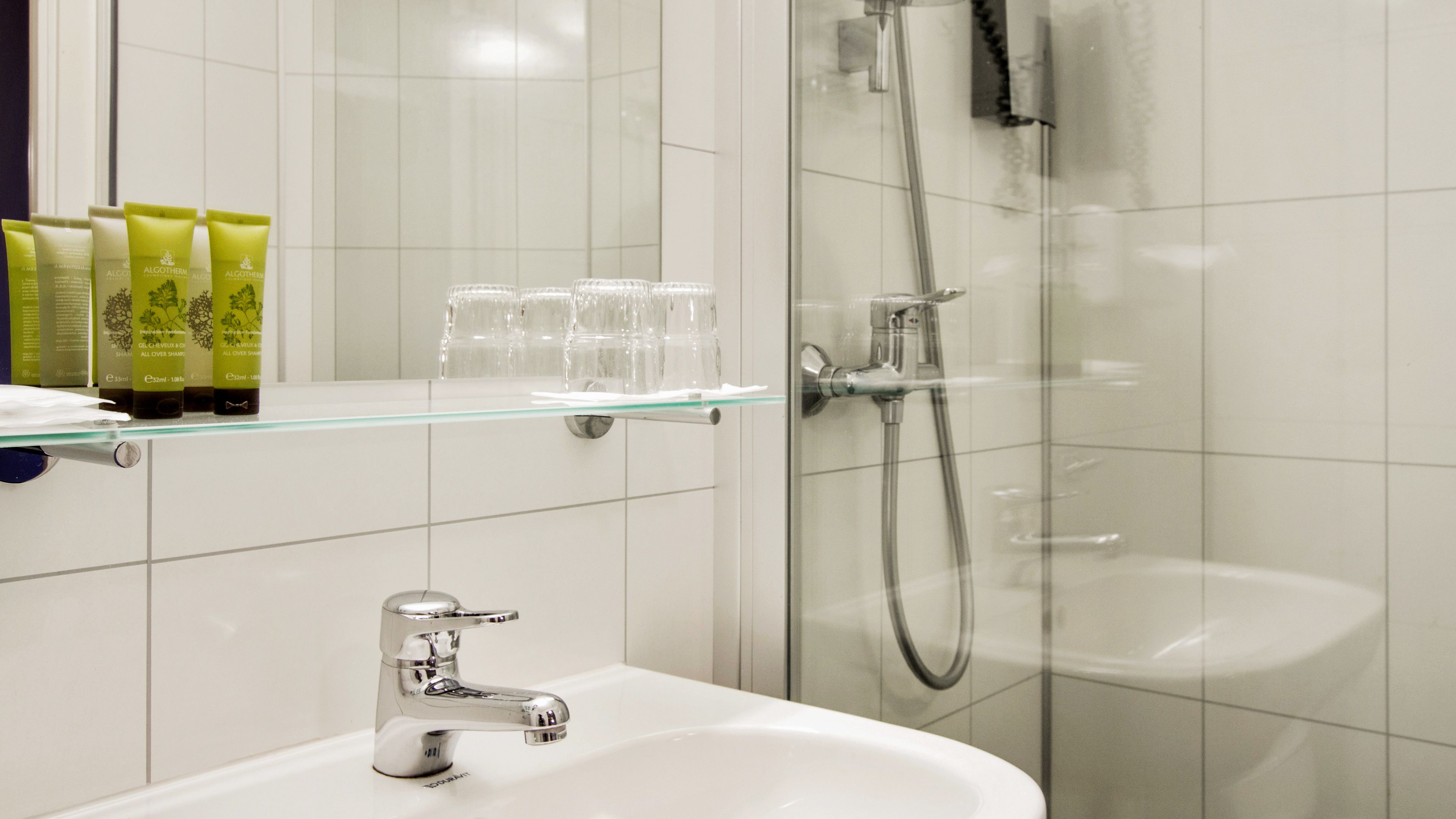 Ein Badezimmer mit Ablagefläche aus Glas, Waschbecken und Dusche.