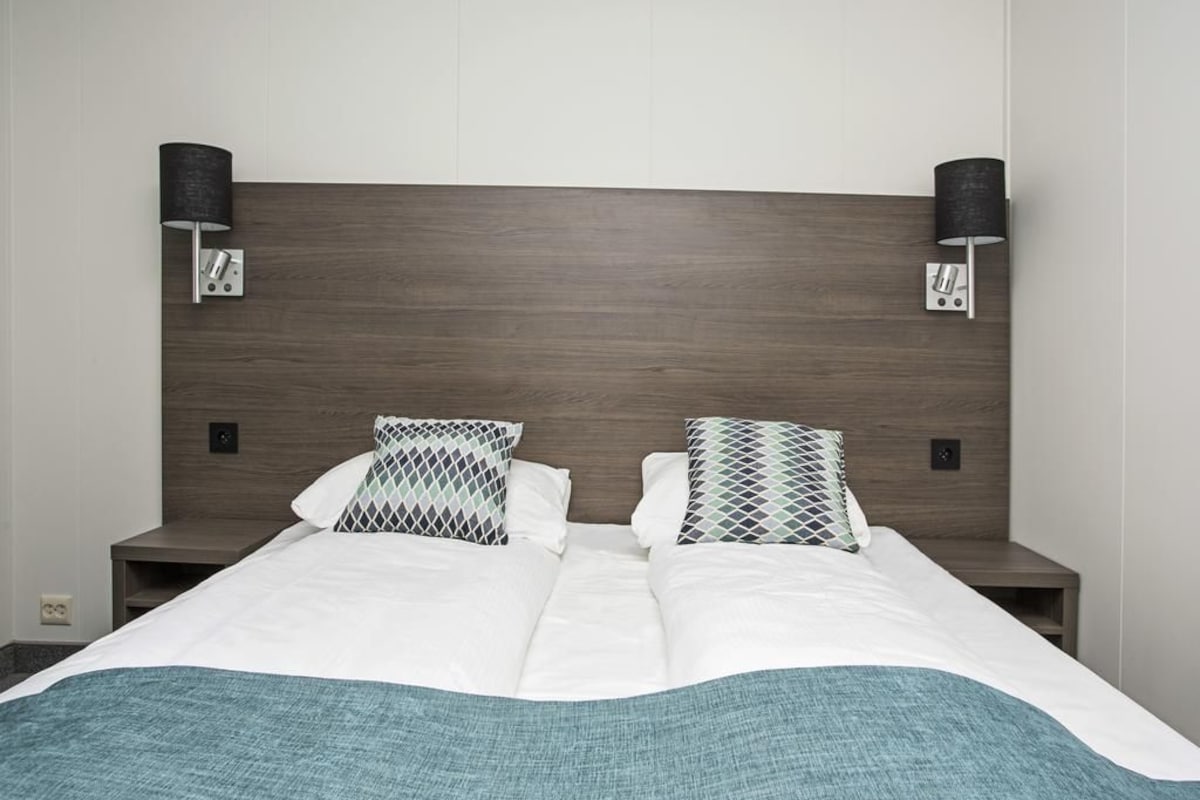 A double bed with a teal throw blanket, two patterned pillows, and two bedside tables with lamps.