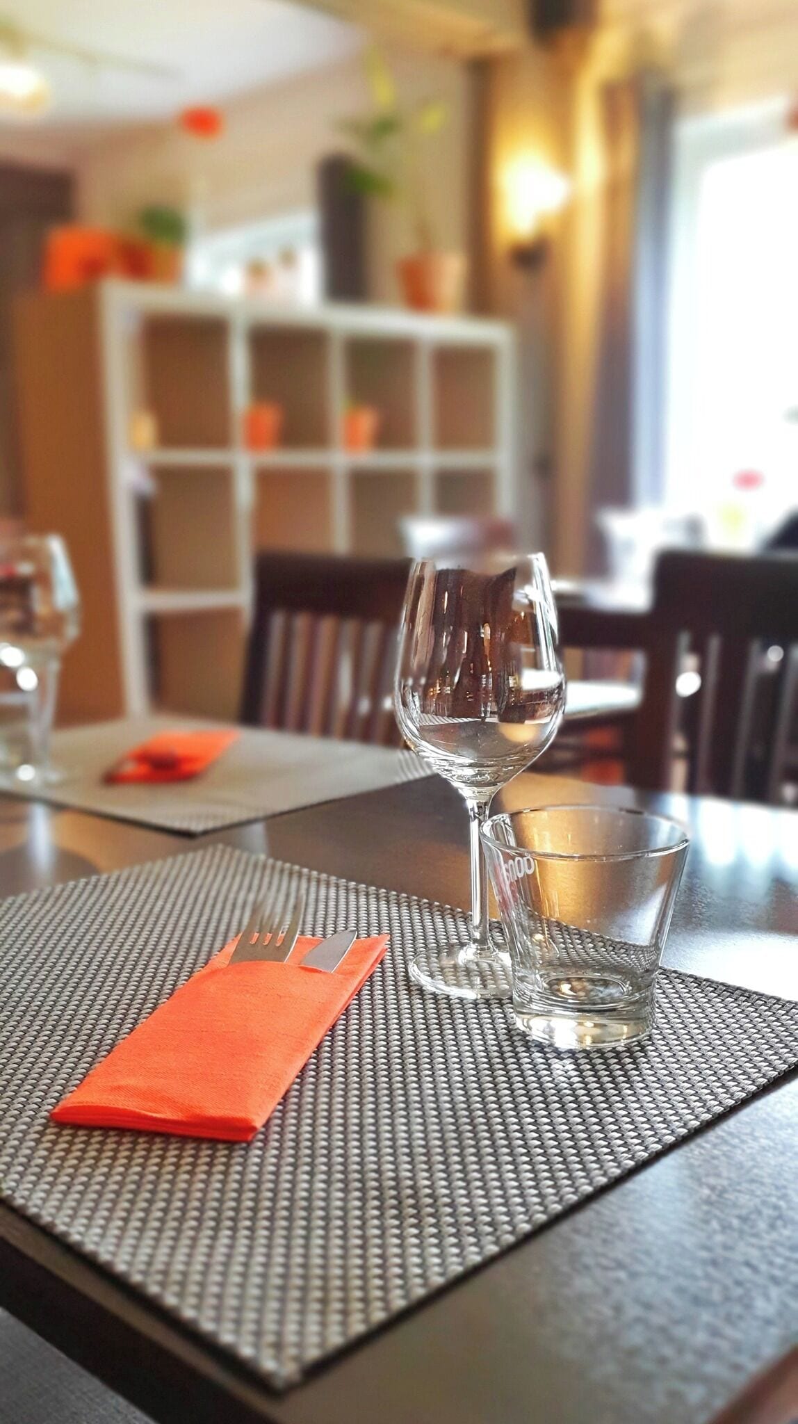A dining table with a clear glass, a folded orange napkin, and a small glass.