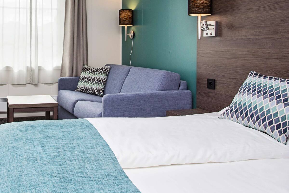 A hotel room with a bed, a sofa, a desk, and a chair.