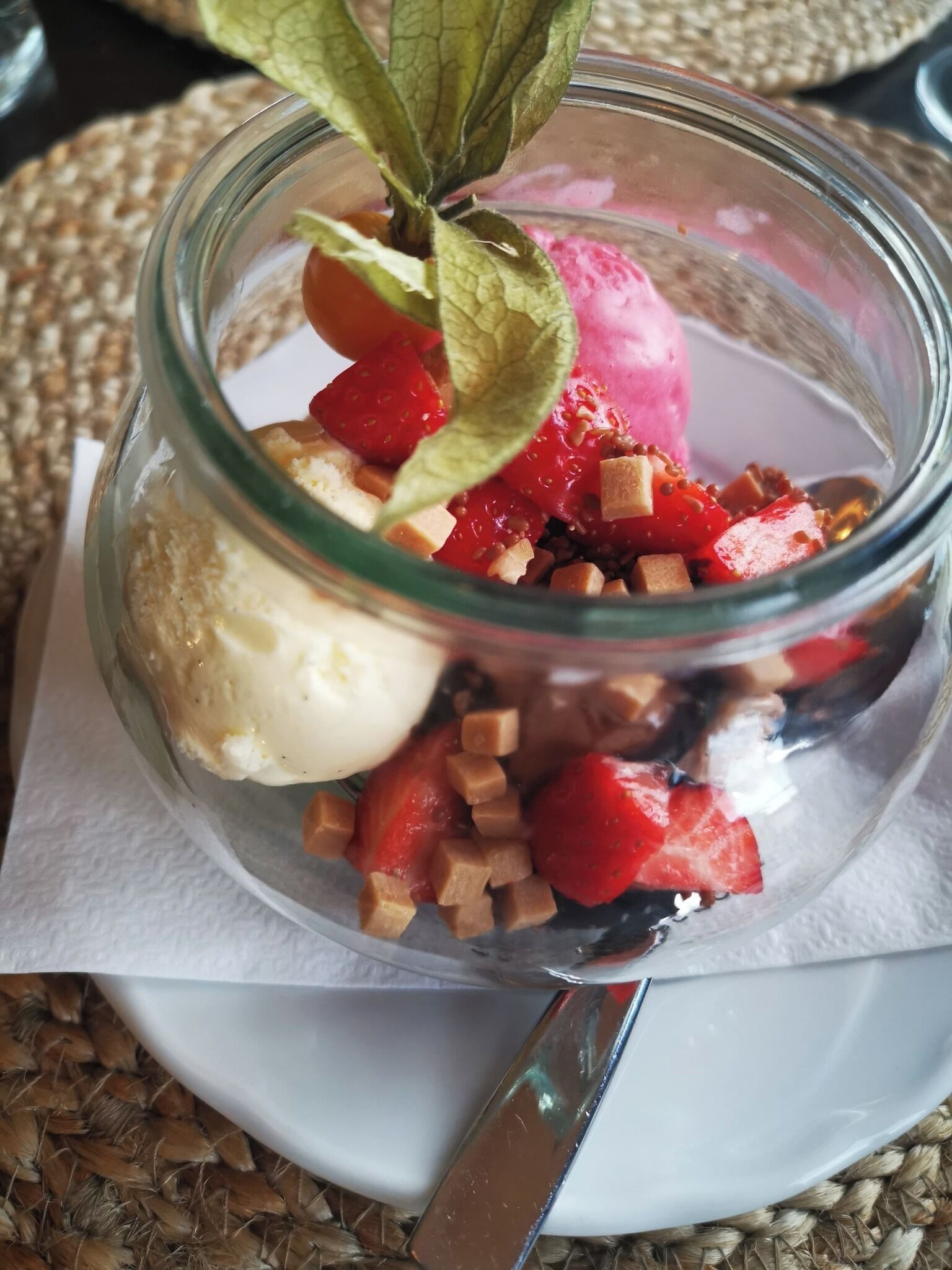 A dessert in a glass jar with strawberries and caramel pieces.