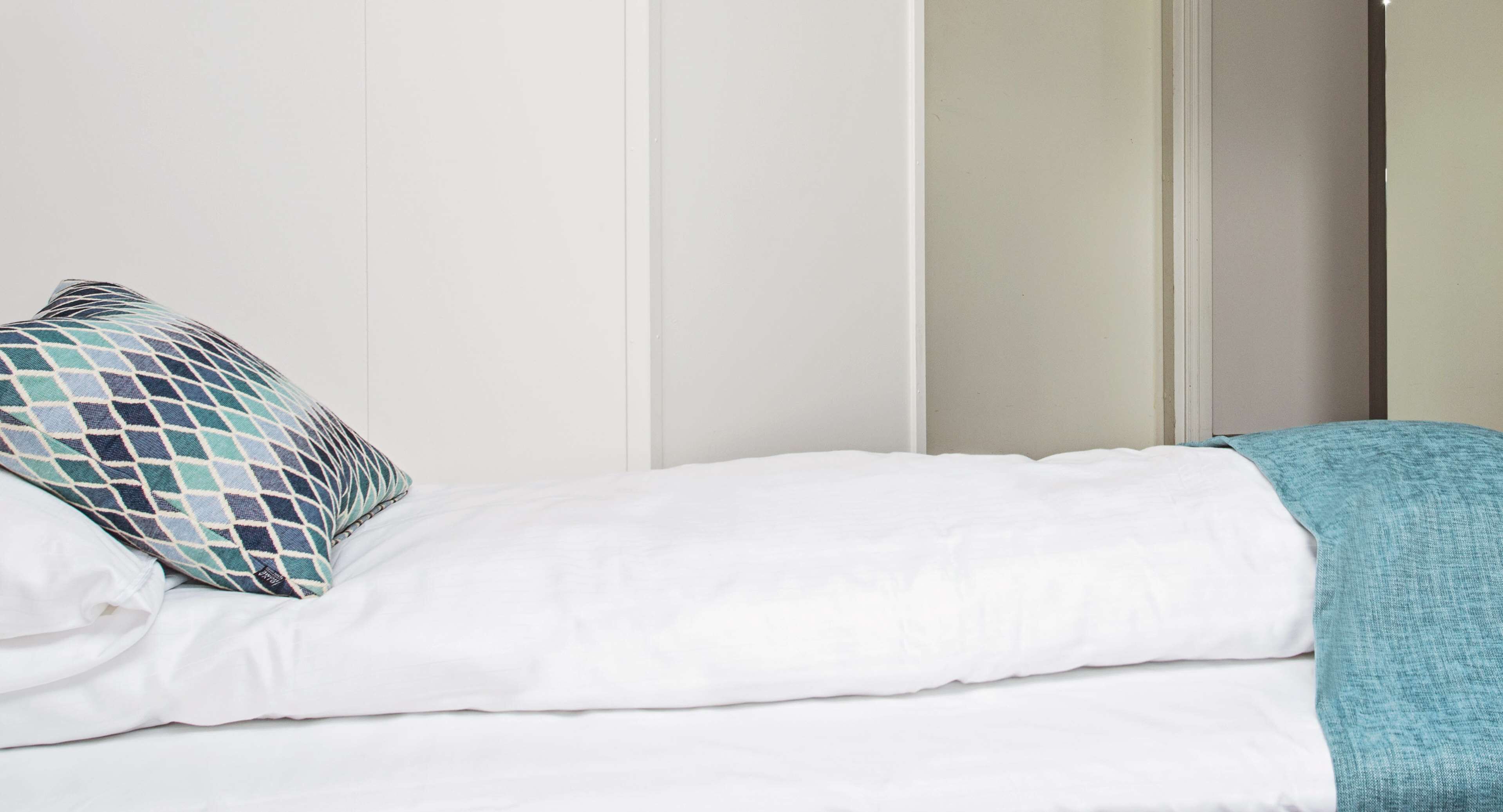 A neatly made bed with white bedding and a blue and white patterned pillow.